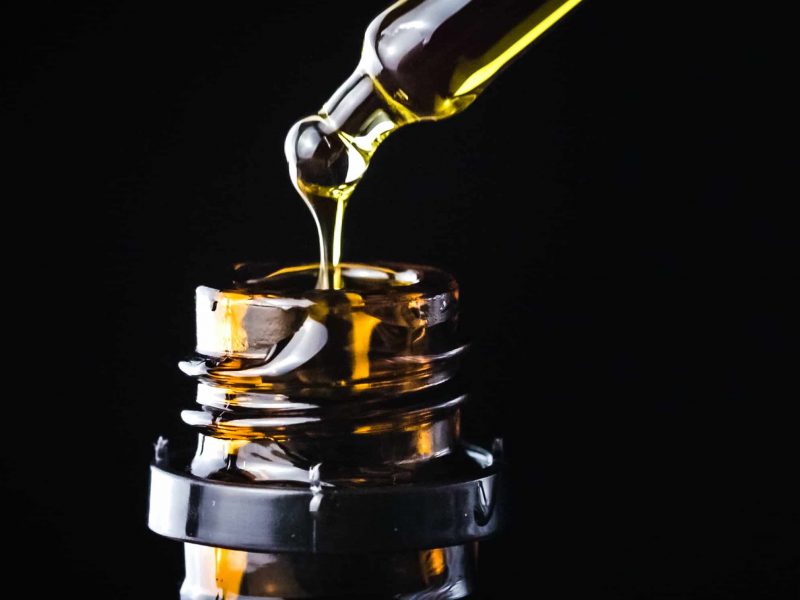 CBD Hemp oil, Hand holding droplet of Cannabis oil against black background. Alternative Medicine